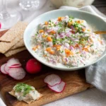 Skål med skärgårdssill toppad med hackad rödlök, dill och Abbas stenbitsrom på en skärbräda med rädisor och knäckebröd