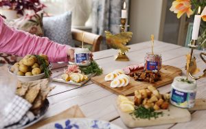 Burkar med Abba Citron- och ramslökssill, Abba, Fransk löksill och Abba Skärgårdssill på ett dukat bord med olika tillbehör som räkor, ägg, gräslök och kavring.